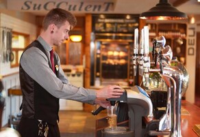 Un barista opera una máquina de café en una cafetería, con una máquina de espresso visible y una taza de café en preparación.