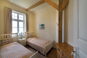 A bedroom with two beds, a nightstand, a wooden dresser, a window with curtains, and a painting on the wall. - Apartment 5 Gut Grubnow Rügen directly on the water for 4 persons (Grubnow)