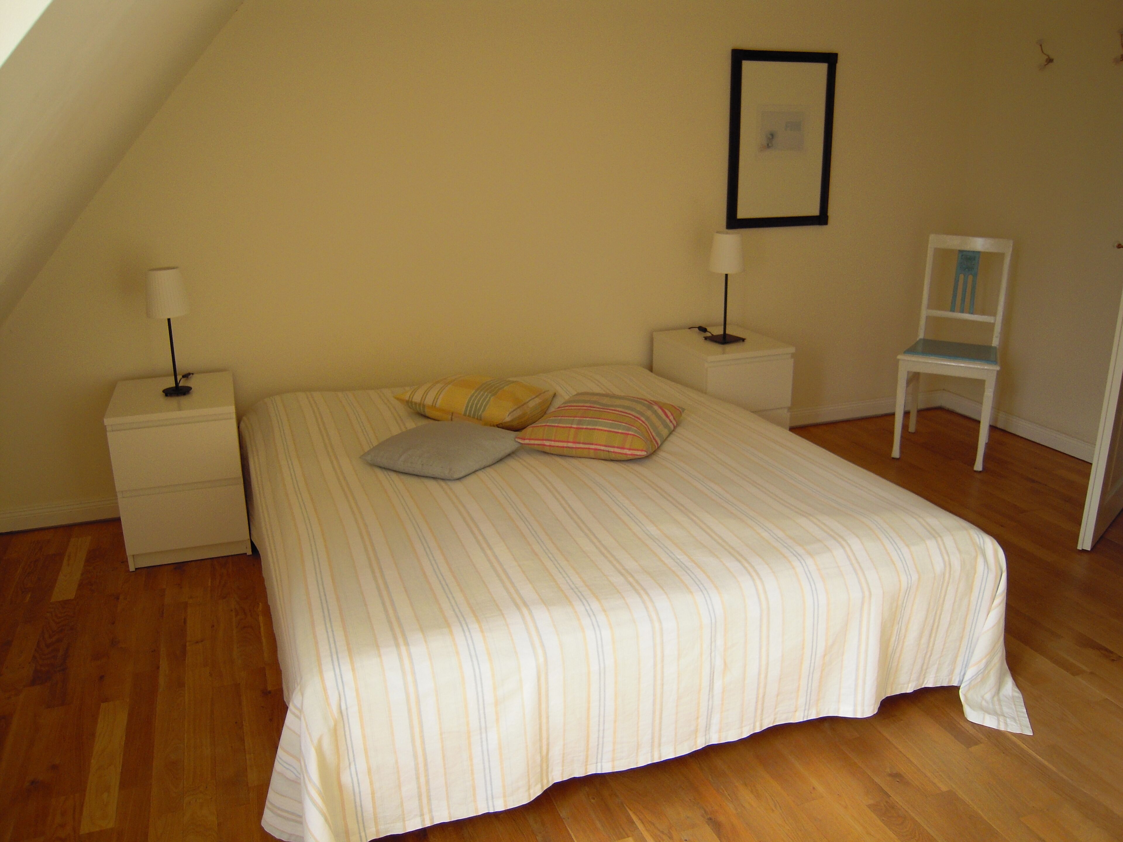 A bedroom with a bed, two bedside tables, a chair, and a picture on the wall.