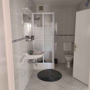 Une salle de bain avec une douche, un lavabo, des toilettes et un petit tapis sur le sol.
