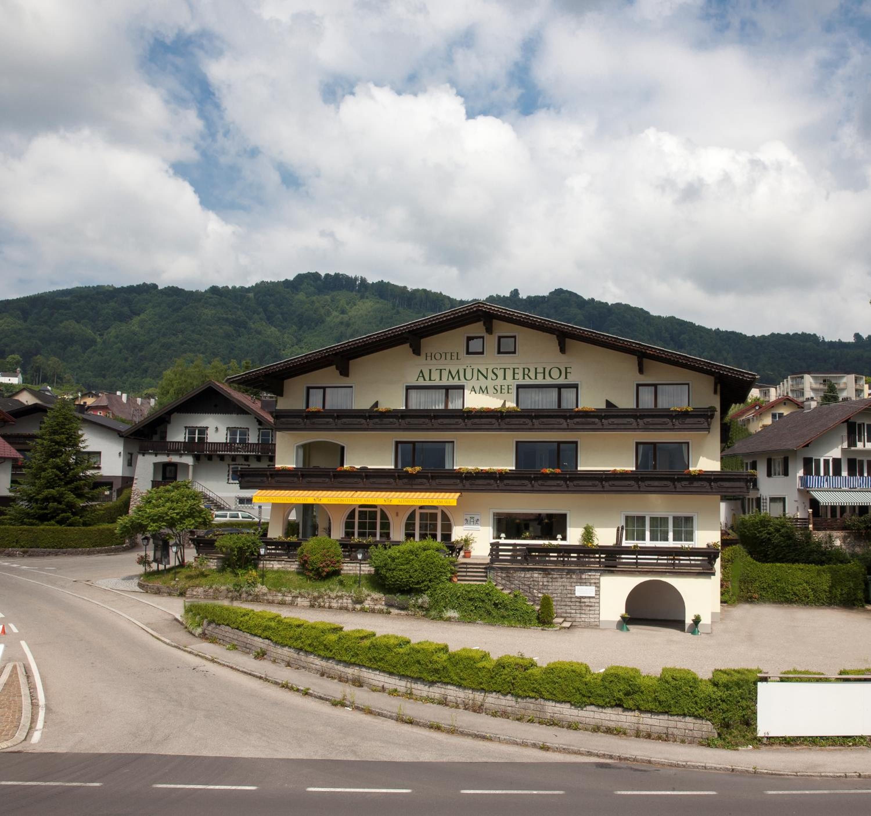 A hotel with a sign reading 'Hotel Almünsterhof Am See' in front of a mountain backdrop.