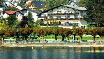 Ein Hotel im traditionellen alpinen Baustil, gelegen am Ufer eines ruhigen Sees mit einem Park im Vordergrund.