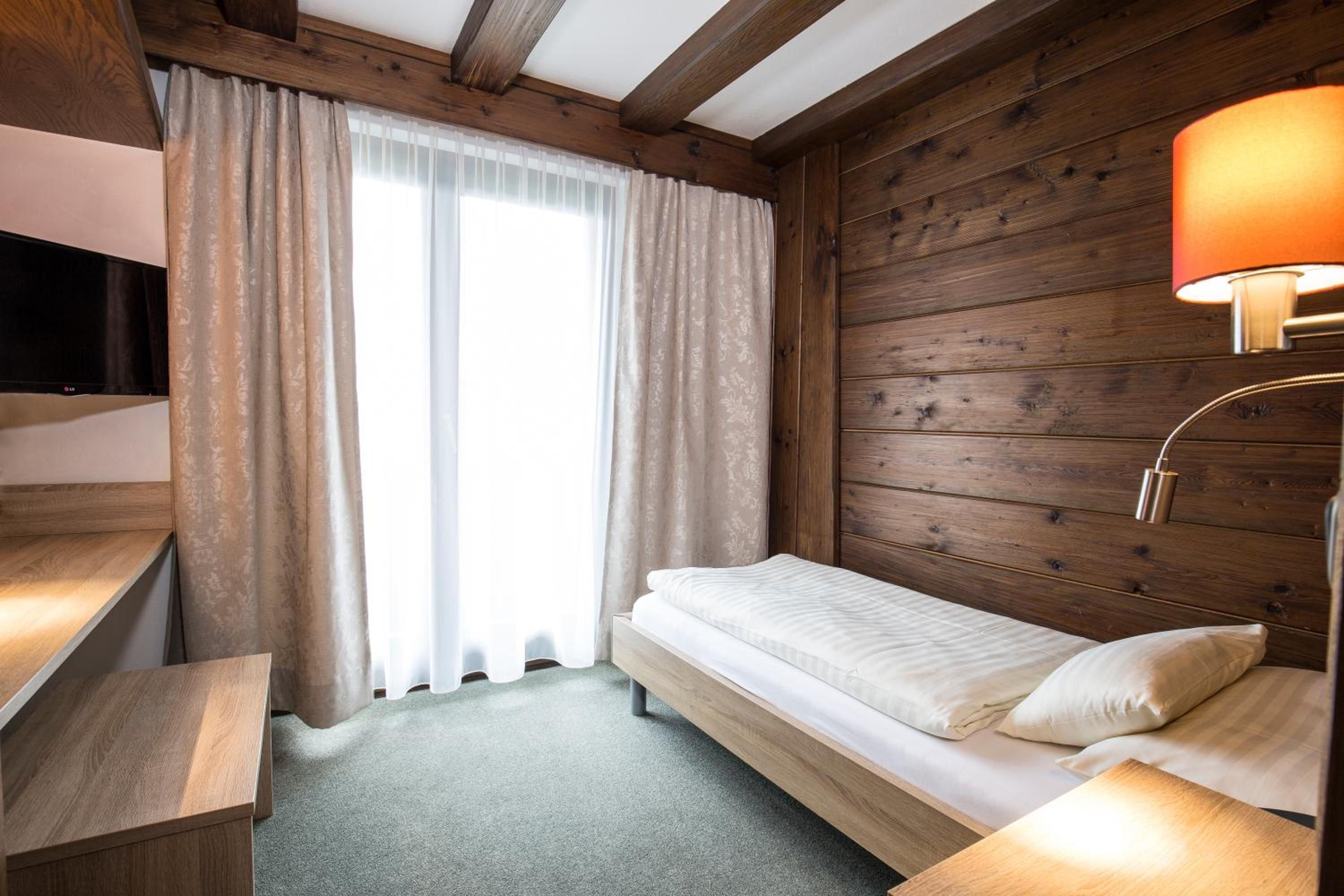 Ein Einzelbett mit Holz-Kopfteil, ein Nachttisch mit Lampe und ein Fernseher an der linken Wand.