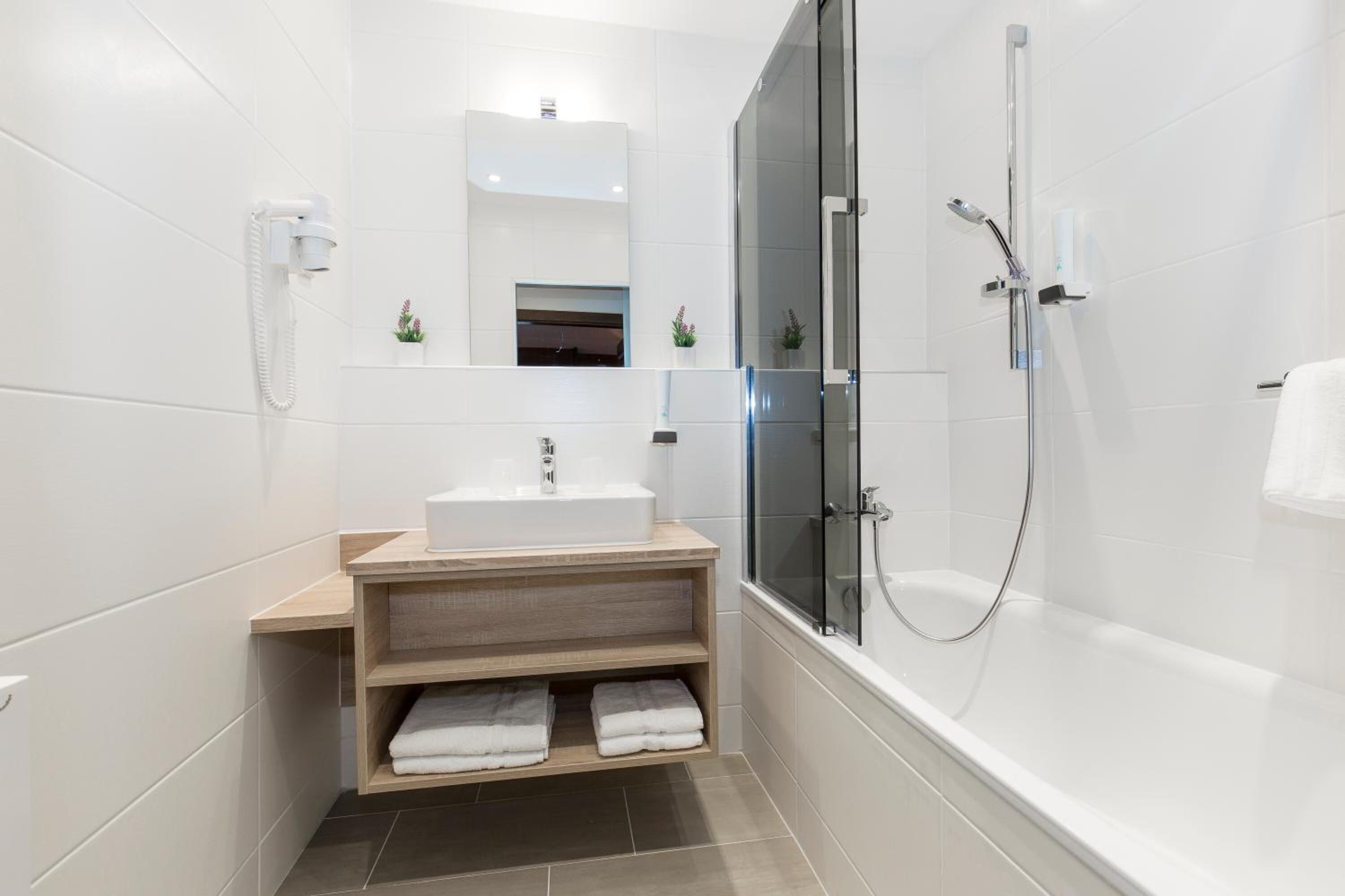 Ein modernes Badezimmer mit Waschbecken, Holzschrank, Duschkabine und Handtuchhalter.