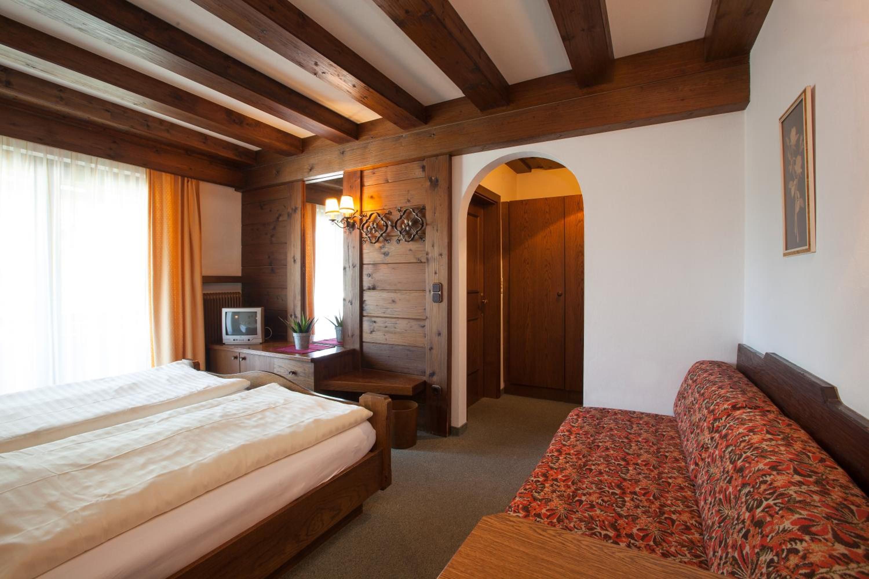 Une chambre à coucher avec un lit, un bureau avec une télévision et une porte en arc donnant sur une autre pièce.