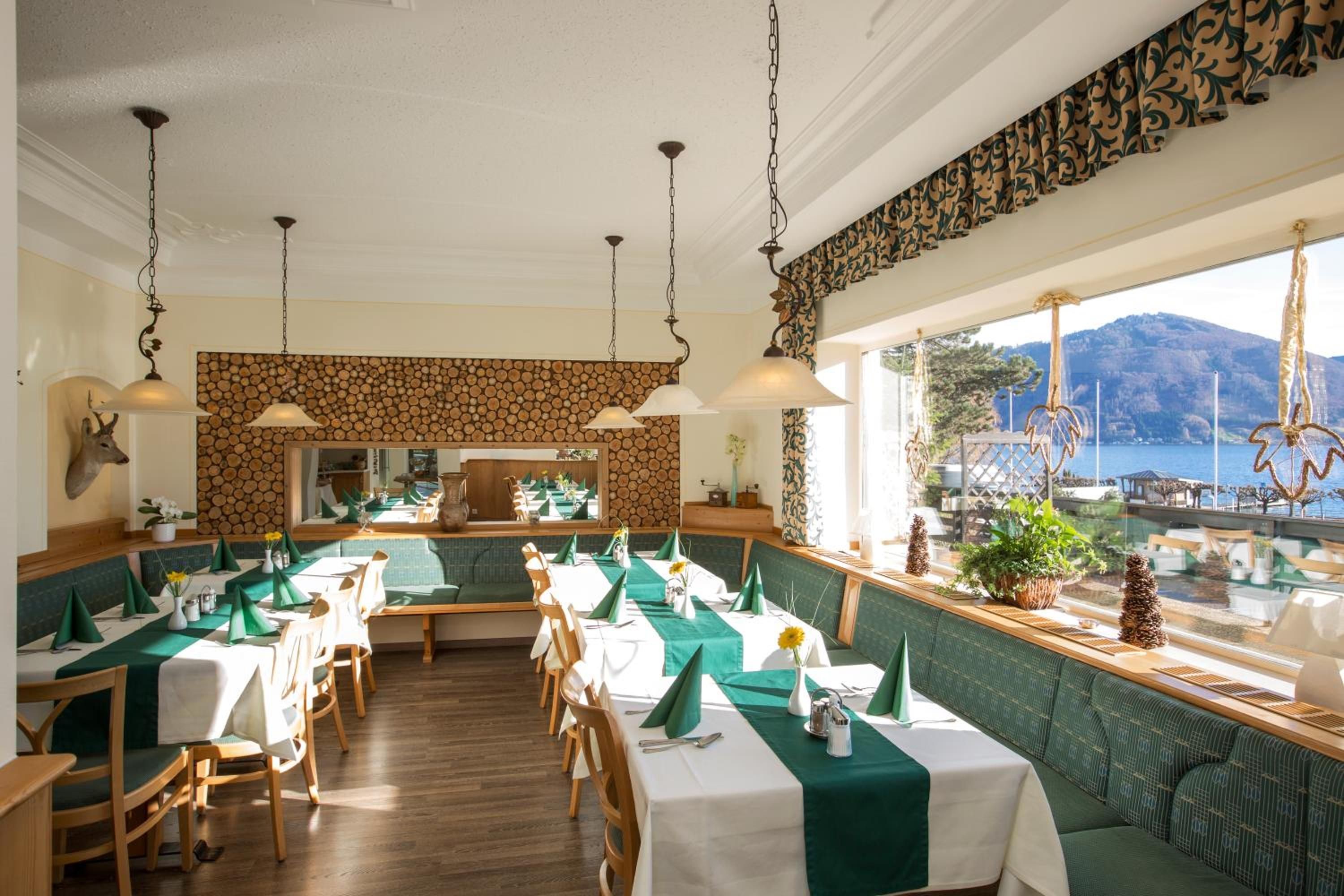 A restaurant with a view of the sea, wooden flooring, and green and white table settings.