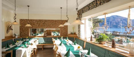 A restaurant with a view of the sea, wooden flooring, and green and white table settings.