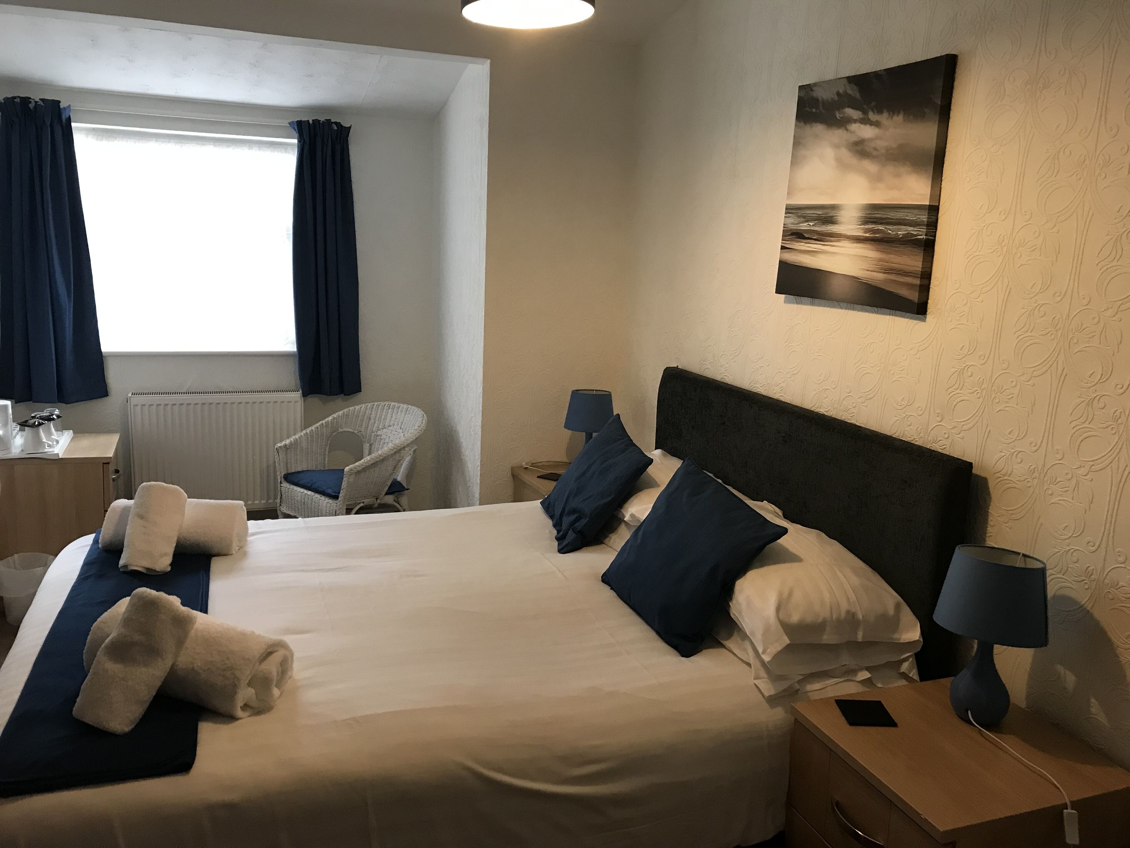 A hotel room with a large bed, a chair, a desk, a lamp, and a painting on the wall.