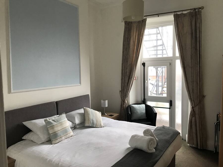 A hotel room with a large bed, a chair, a desk, and a window with curtains.