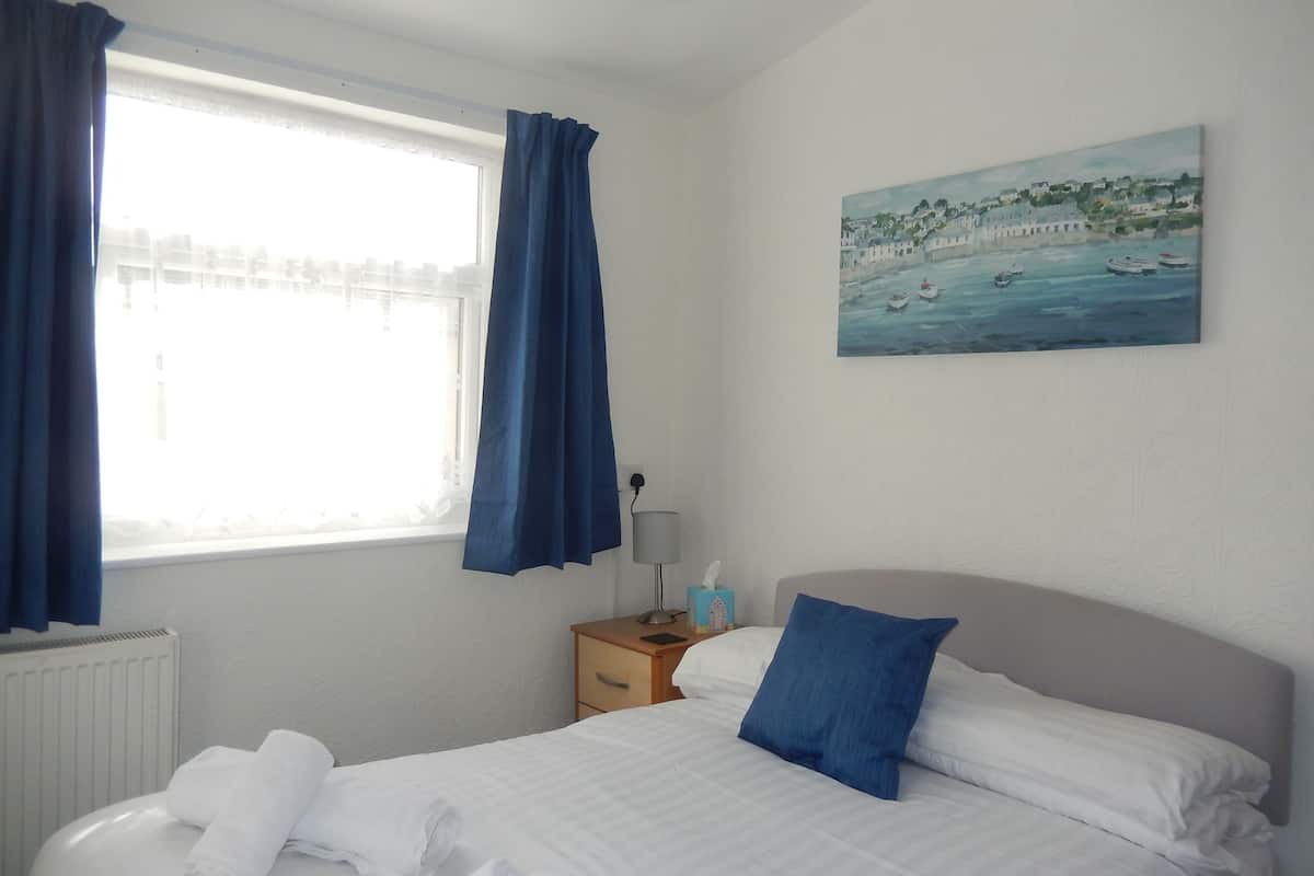 Quarto de hotel com cama, mesa de cabeceira, um quadro e janela com cortinas.