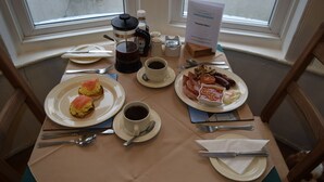 Una mesa de desayuno dispuesta con platos de comida, tazas de café y un cartel con el menú.