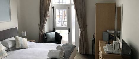 Una habitación de hotel con cama, escritorio, silla, espejo y ventana con cortinas.