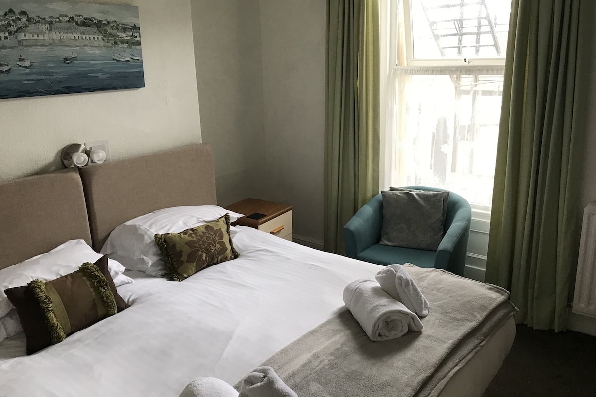 Quarto de hotel com cama, mesa de cabeceira, cadeira e um quadro na parede.