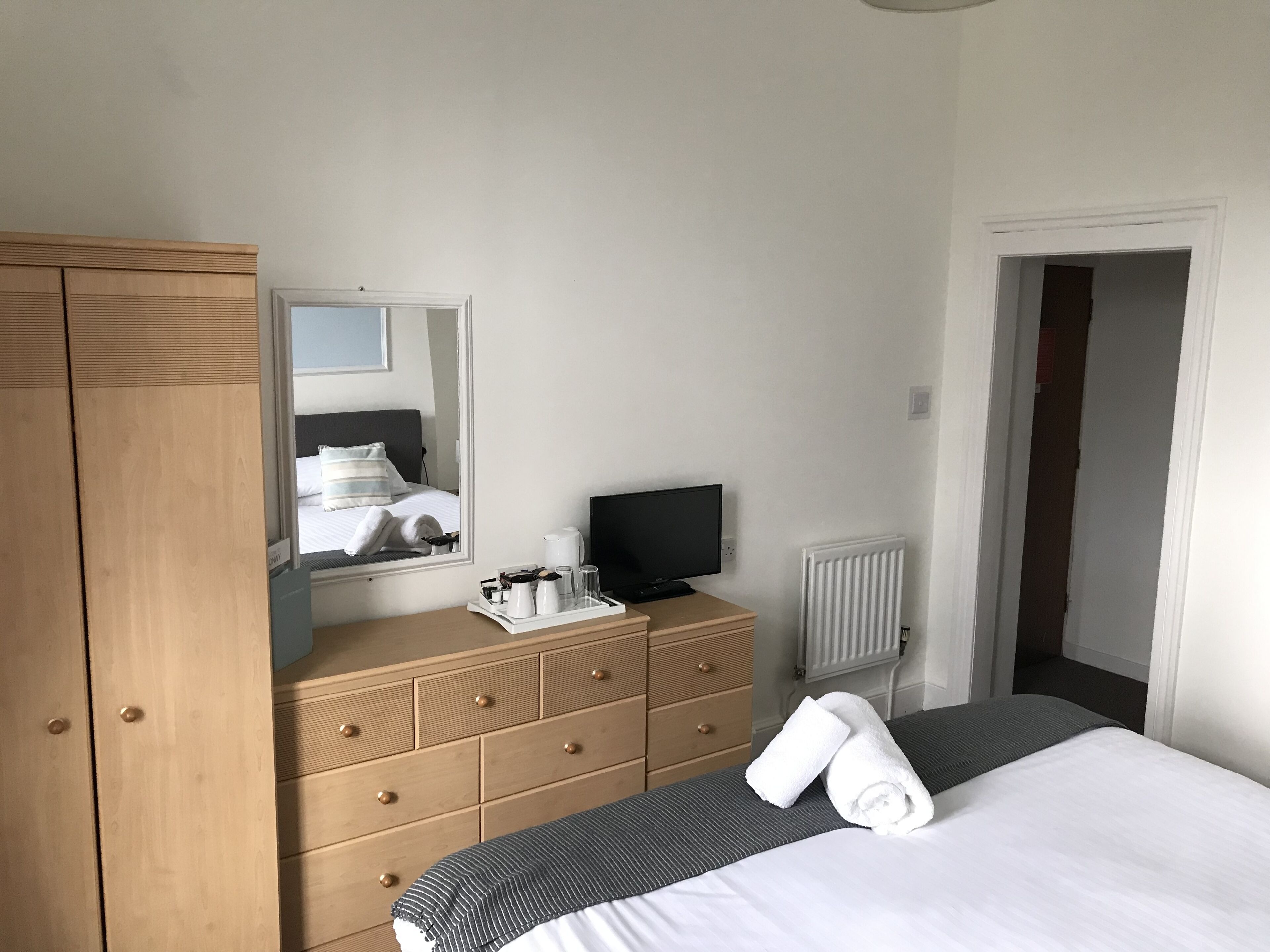 A hotel room with a bed, a wooden dresser, a television, and a mirror.