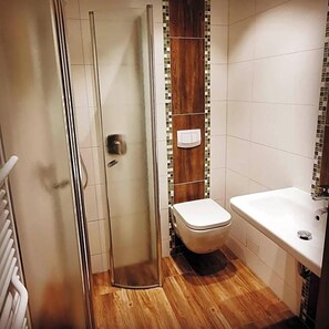 A bathroom with a glass shower enclosure, a toilet, and a sink.