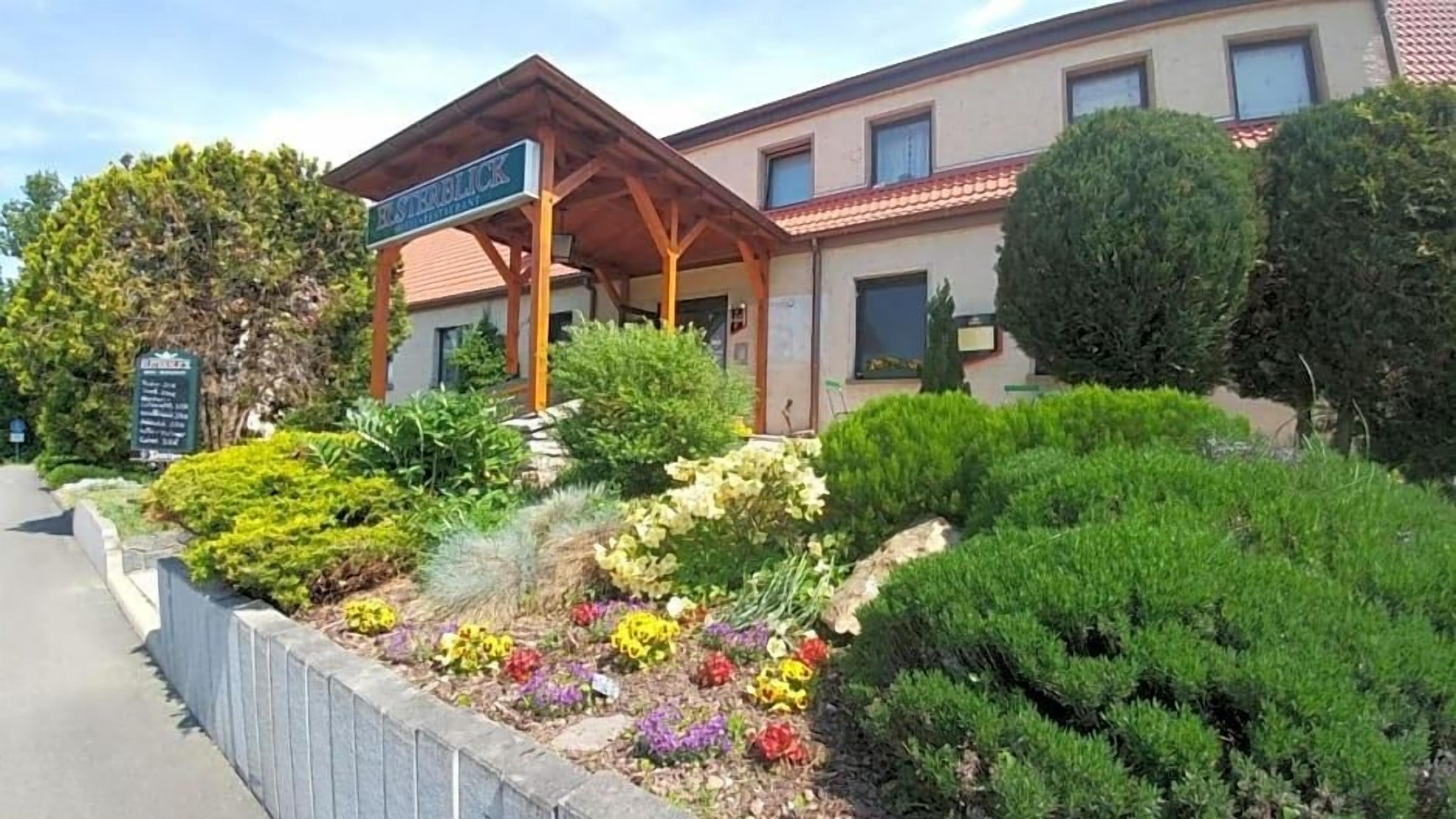 A building with a covered entrance, a landscaped garden with various plants, and a signboard.