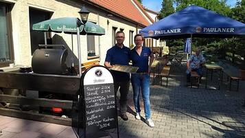 A food vendor setup with a menu board and two people standing beside it.