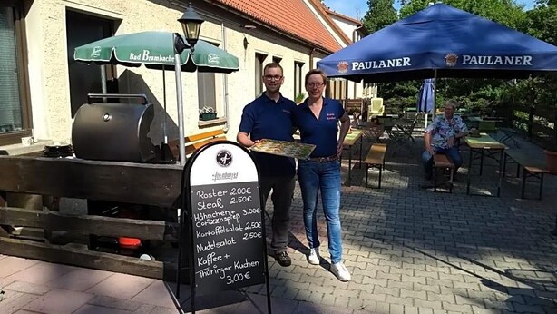 A food vendor setup with a menu board and two people standing beside it.