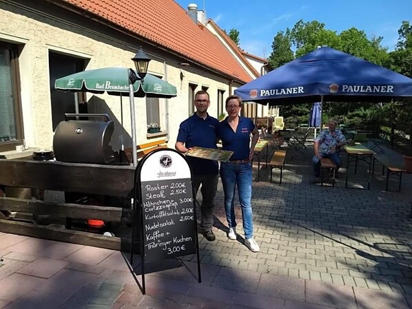 A food vendor setup with a menu board and two people standing beside it.