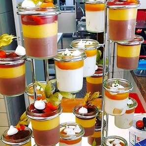 A variety of layered desserts in glass jars, some with whipped cream on top, displayed on a metal stand.