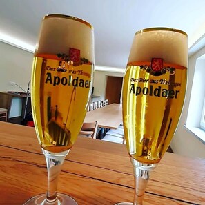 Dos vasos de cerveza Apoldaer sobre una mesa de madera en una habitación con una ventana y una puerta al fondo.