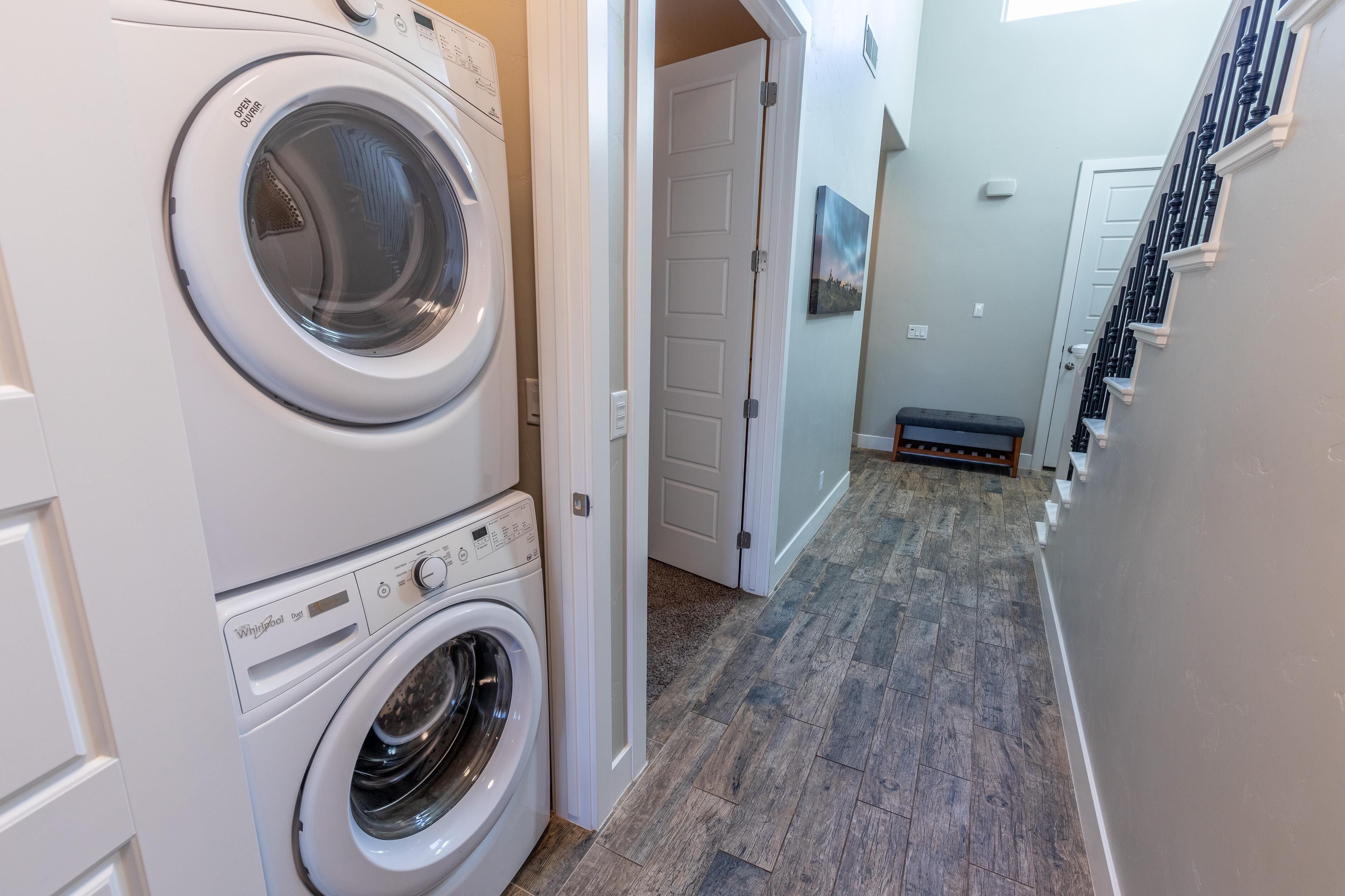 A laundry room with two stacked washers and dryers, a wooden floor, and a door leading to another room.