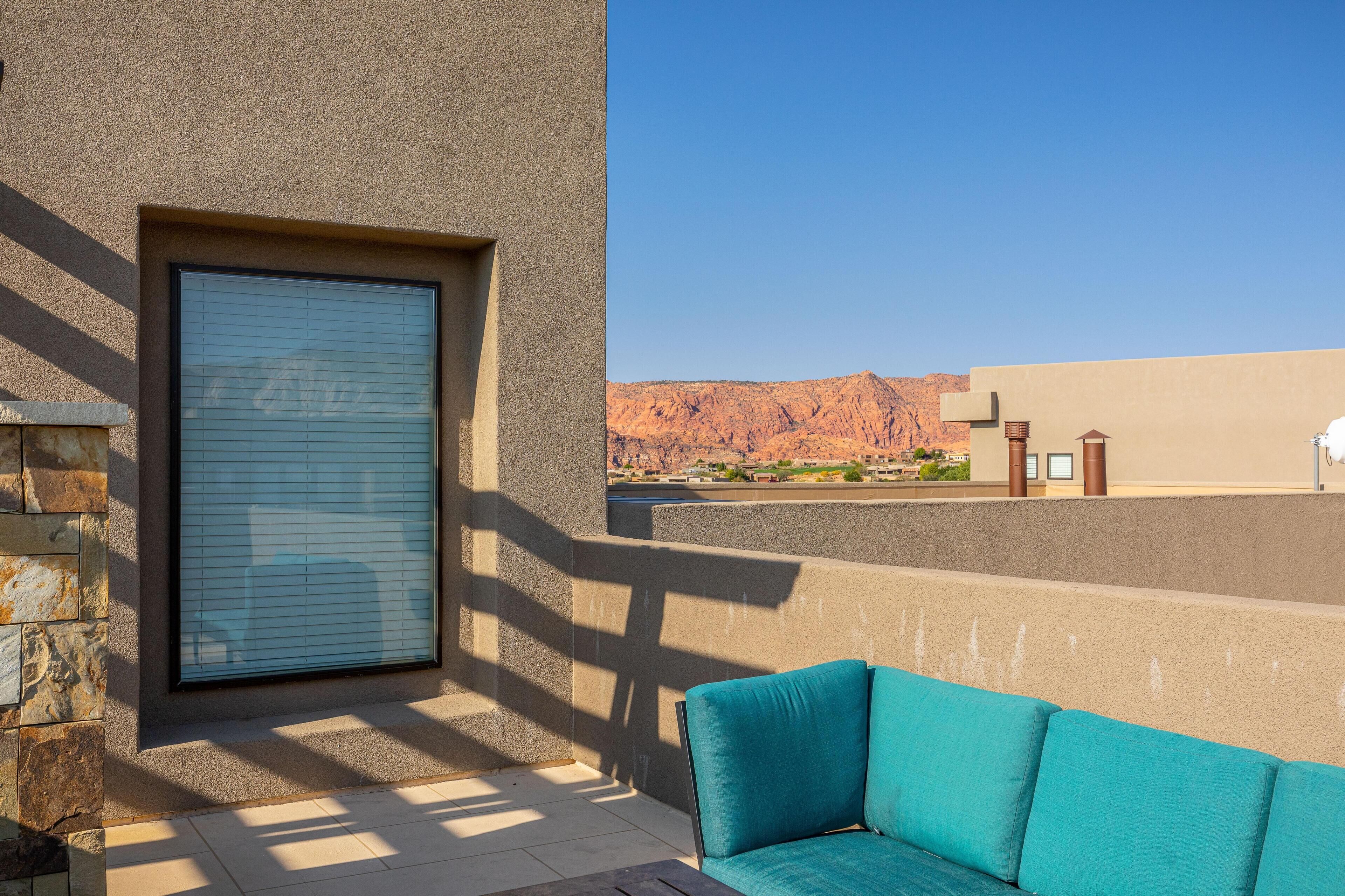 A balcony with a blue cushioned seating area, a closed window, and a view of a desert landscape.