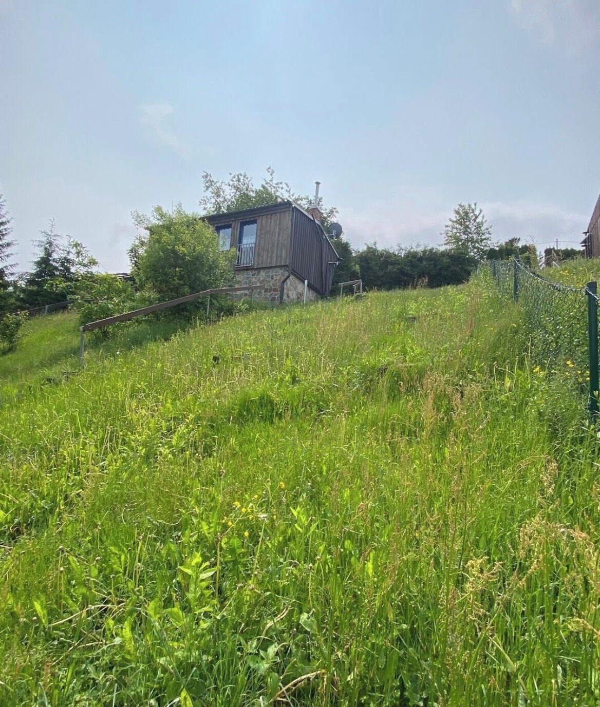 A rustic house with a stone foundation and wooden upper structure, surrounded by lush green fields and a clear sky.