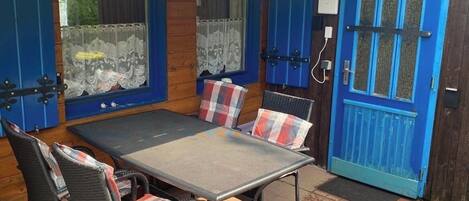 Un patio al aire libre con una mesa y sillas de metal, puertas azules y paredes de madera.