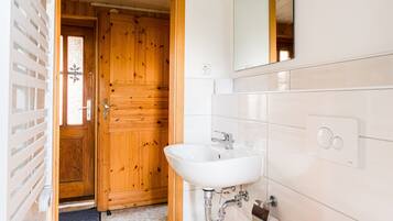 A bathroom with a wooden door, white tiles, a sink, and a mirror.