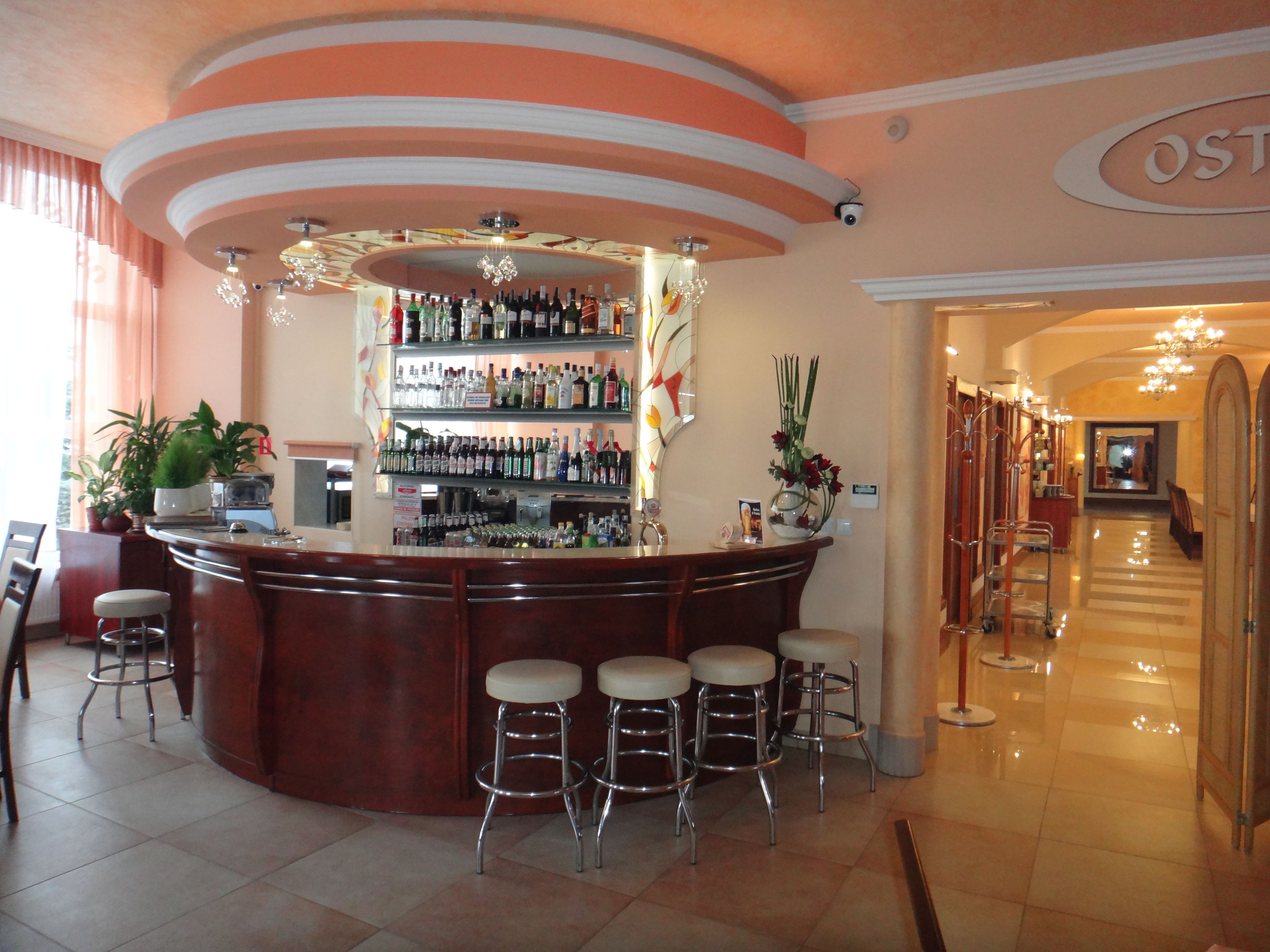 Zona de bar con mostrador curvo, varios taburetes y una gran variedad de botellas.