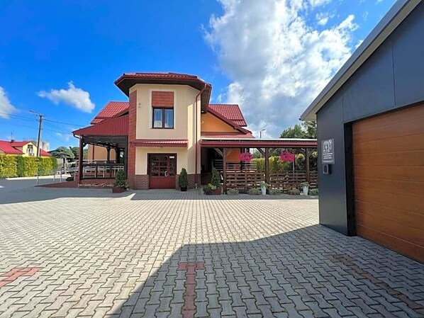 A two-story house with a red roof, a covered porch, and a paved driveway.