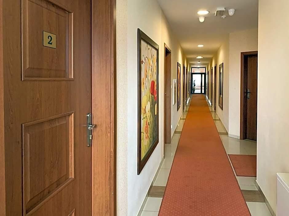 A hotel hallway with wooden doors, numbered room signs, and a red carpet.