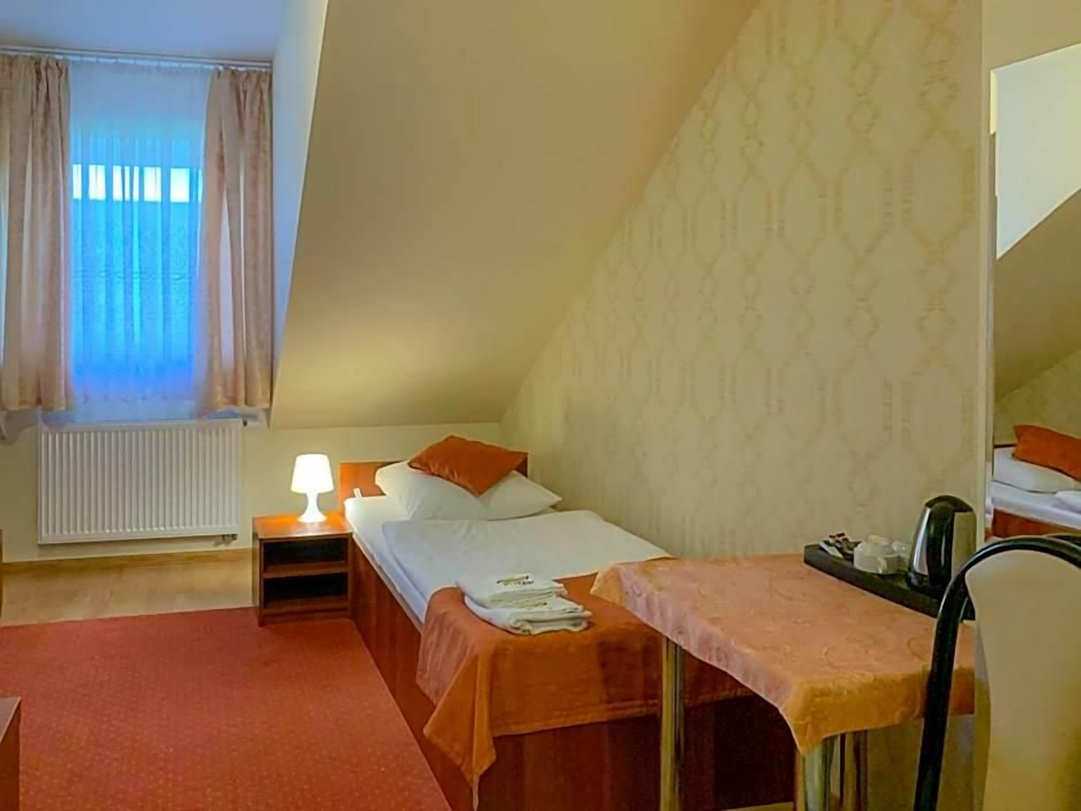 A bedroom with a bed, bedside table, lamp, and a small table with a chair.