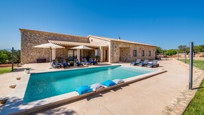 Una villa de piedra con piscina, sillas de descanso y sombrillas.