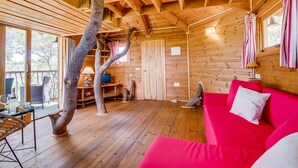 Interior acogedor de una cabaña con piso de madera, un sofá rojo, un televisor y un ventanal con vistas a un paisaje natural.