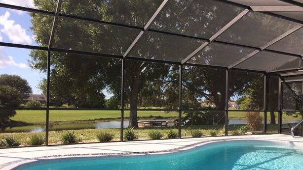 A covered outdoor swimming pool with lounge chairs and a view of a grassy area and trees.