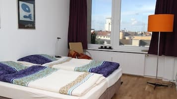 Ein Hotelzimmer mit zwei Betten, einem Fenster mit Blick auf Gebäude, einer Lampe und einem Bild an der Wand.