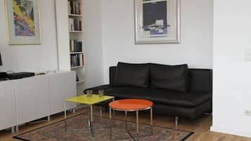 Ein Wohnzimmer mit einem schwarzen Sofa, einem gelben Couchtisch, einem roten Beistelltisch, einer weißen Kommode und einem Bücherregal.