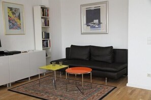 Een woonkamer met een zwarte bank, een gele salontafel, een rode bijzettafel, een witte kast en een boekenkast.