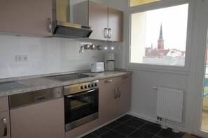 Een compacte keuken met roestvrijstalen apparatuur, een raam met uitzicht op een stadsbeeld en een witte radiator.
