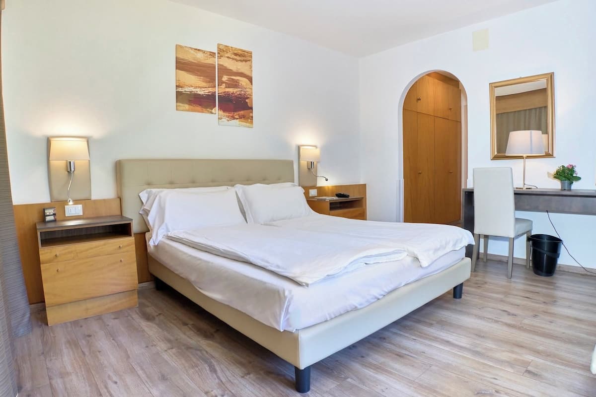 Une chambre d’hôtel comprenant un lit, des tables de chevet, un bureau, une chaise, un miroir et des œuvres d’art accrochées au mur.