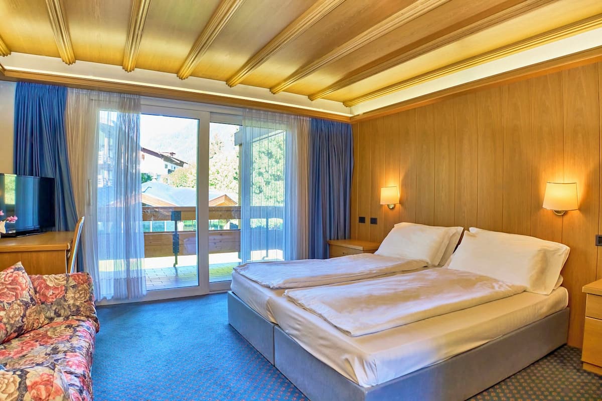 Une chambre d’hôtel avec un lit double, un téléviseur posé sur une table en bois et une vue sur un immeuble à travers de grandes fenêtres.