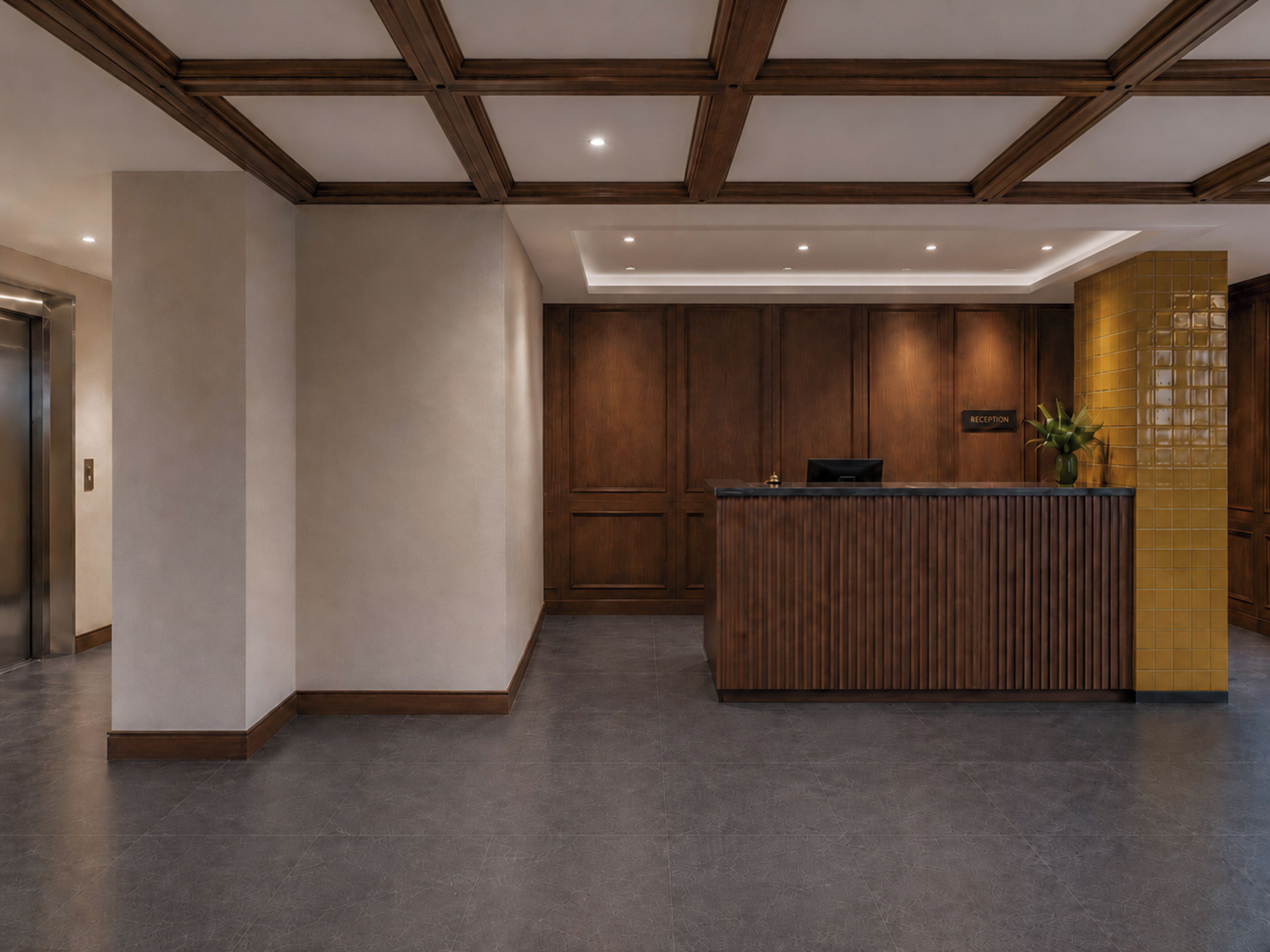 Una reception con scrivania in legno, zona accoglienza con parete rivestita in piastrelle e soffitto con travi in legno.