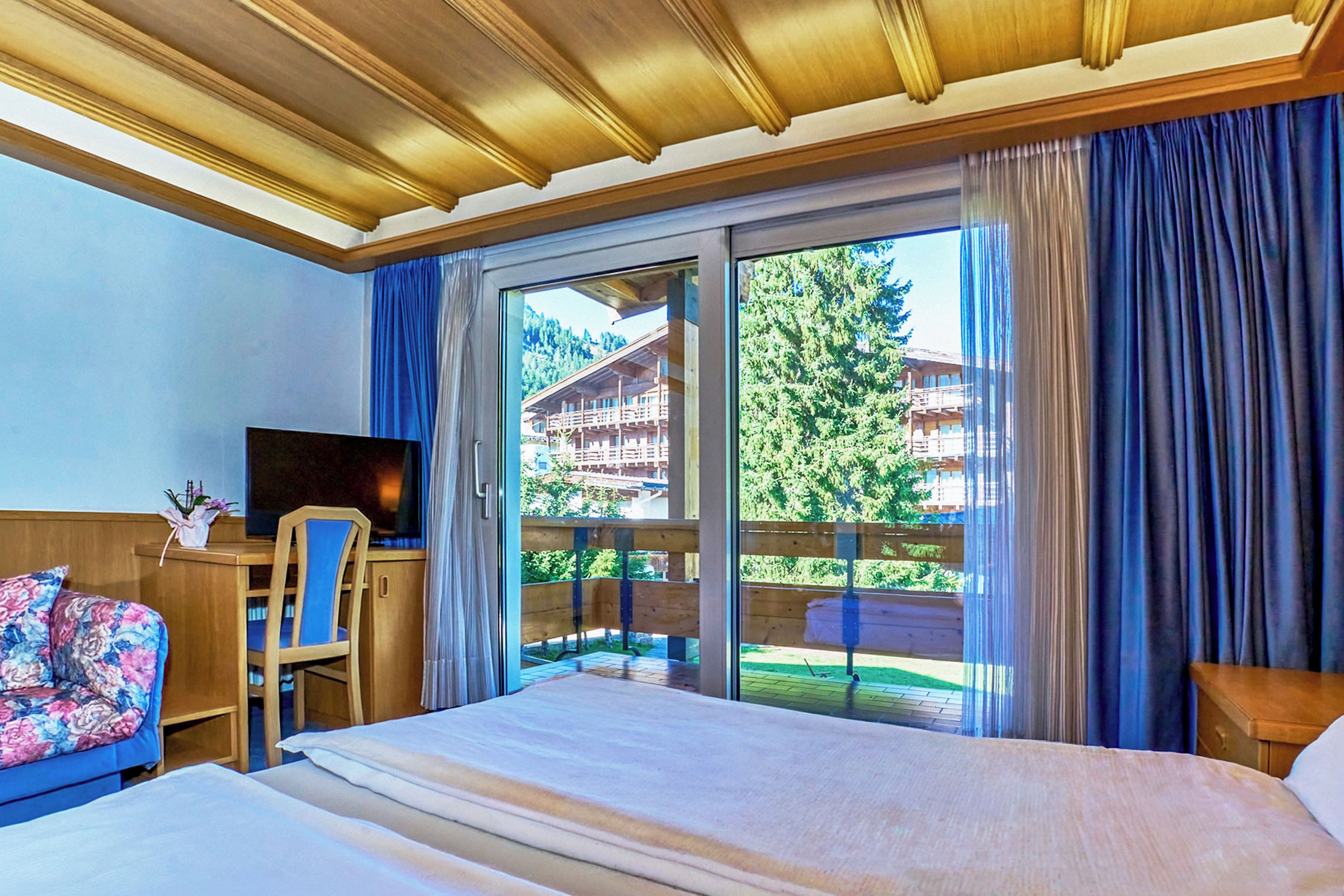 Camera d'albergo con un letto, una scrivania con una sedia, una televisione e vista su un edificio e degli alberi dalla finestra.