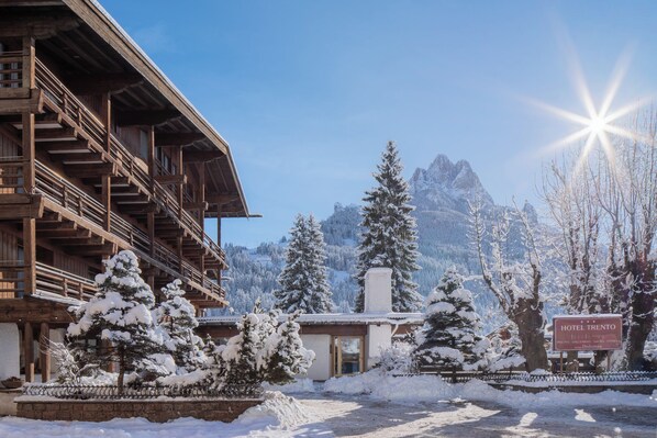 A wooden building with a balcony, surrounded by snow-covered trees and mountains in the background. - Hotel Trento Dolomites Affiliated by Melia (Pozza di Fassa)