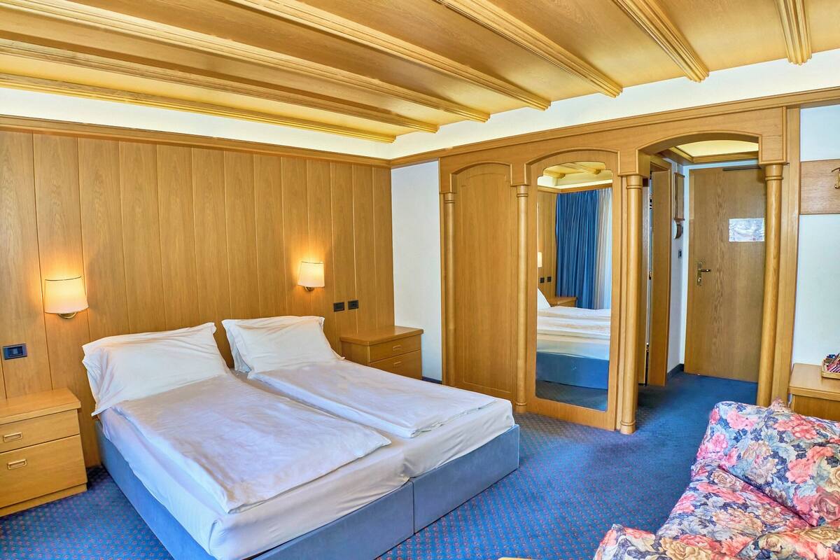 Une chambre d’hôtel avec un grand lit, des boiseries, un miroir et un canapé à motifs floraux.