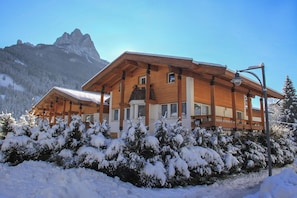 Un chalet en bois, doté d’un toit en pente, entouré d’arbres couverts de neige et avec une montagne en arrière-plan.