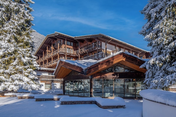A wooden chalet with a balcony and large windows, surrounded by snow-covered trees.