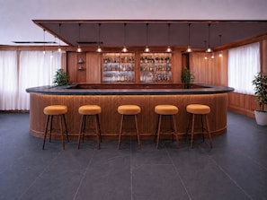 A bar area with a curved counter, five stools, and a shelf of bottles.